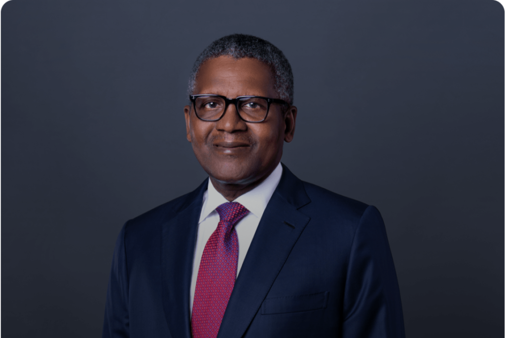 Aliko dangote wearing glasses and a suit with a red tie smiling confidently in a formal portrait