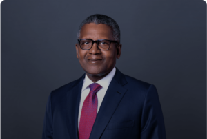 Aliko Dangote, wearing glasses and a suit with a red tie, smiling confidently in a formal portrait.