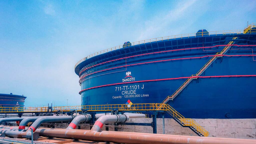 Large blue storage tanks at the Dangote Refinery, labeled 'CRUDE' with a capacity of 120 million litres, connected by pipelines.