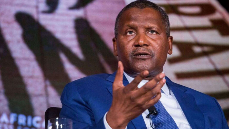Aliko Dangote, CEO of Dangote Group, speaking at a business forum, wearing a blue suit and gesturing with his hand
