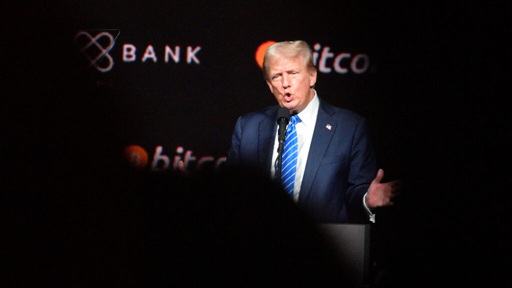 Donald trump speaking at the bitcoin2024 conference in nashville wearing a blue suit and striped tie with the bitcoin logo in the background