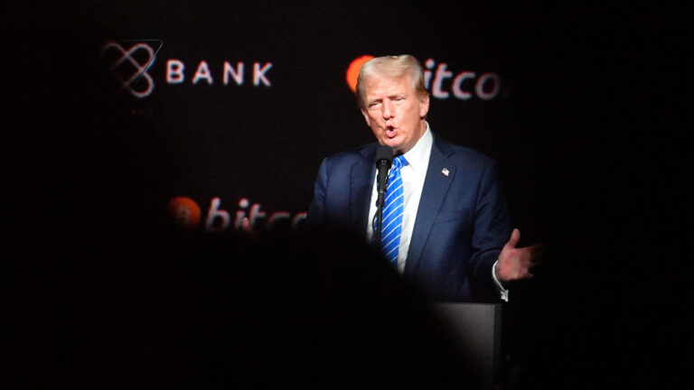 Donald Trump speaking at the Bitcoin2024 Conference in Nashville, wearing a blue suit and striped tie, with the Bitcoin logo in the background.