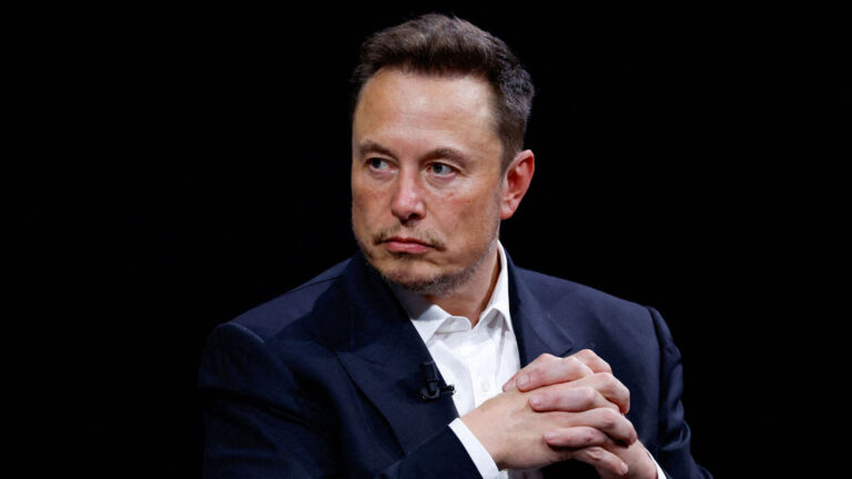 Elon Musk, Chief Executive Officer of SpaceX and Tesla, and owner of X, sits with his hands clasped, looking serious during an event.
