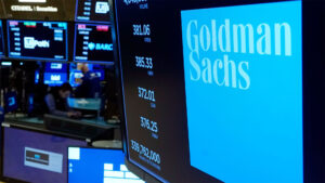 An electronic display shows the Goldman Sachs logo and stock information on the trading floor, highlighting the financial firm's presence in the market.