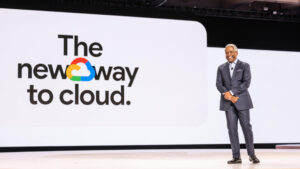 Thomas kurian ceo of google cloud standing on stage in front of a large screen displaying the phrase the new way to cloud during a company presentation