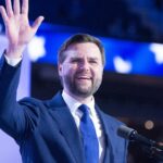 J D Vance wearing a blue suit and tie waves to the audience while speaking at the 2024 republican national convention The background features a patriotic display with stars emphasizing the events significance