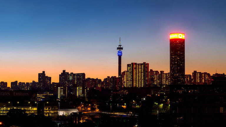 A stunning view of the Johannesburg skyline at dusk, featuring the iconic Hillbrow Tower and illuminated buildings against a vibrant sunset backdrop.