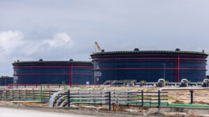 Large oil storage tanks at the Dangote Refinery in Nigeria, with a crane and pipelines visible.