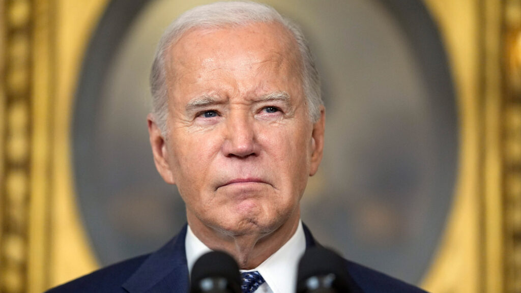 President joe biden giving a serious speech with a focused expression and microphones in front of him