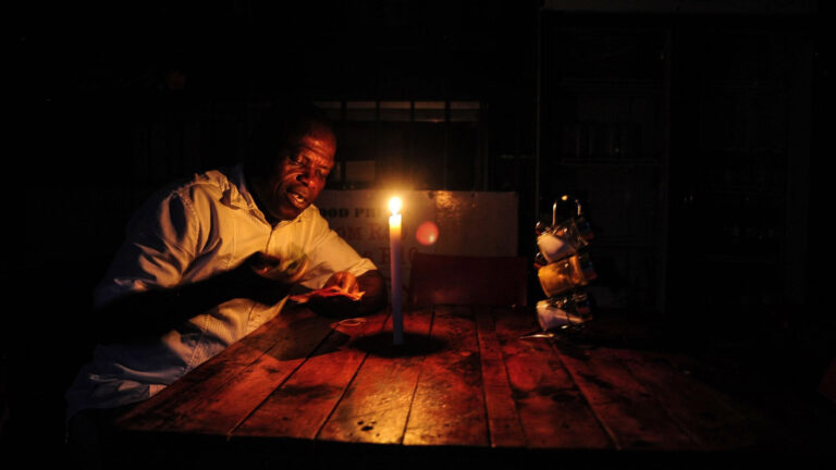 A restaurant owner counting banknotes by candlelight during a power outage in South Africa. Credit: Leon Sadiki/Bloomberg.