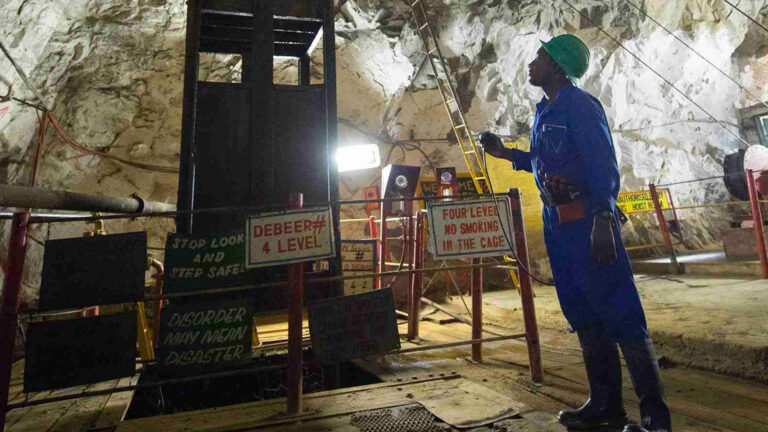 A Sandawana Mines worker inspects an underground mining shaft, surrounded by various safety signs, emphasizing the importance of safety protocols in mining operations.
