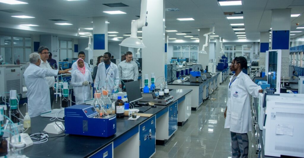 Staff members in lab coats engaged in a discussion inside a modern laboratory at the Dangote Refinery, surrounded by scientific equipment and workstations.