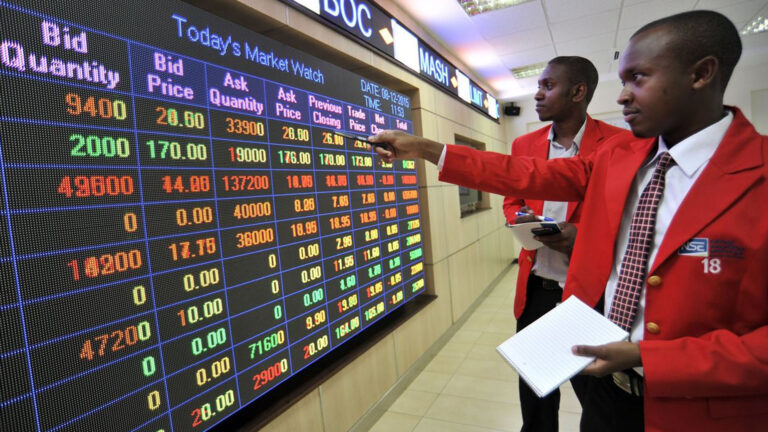 Traders in red jackets analyzing stock market data on an electronic display at the Nairobi Securities Exchange.