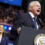 Gov Tim walz speaking at a podium with vice president kamala harris smiling behind him at a rally