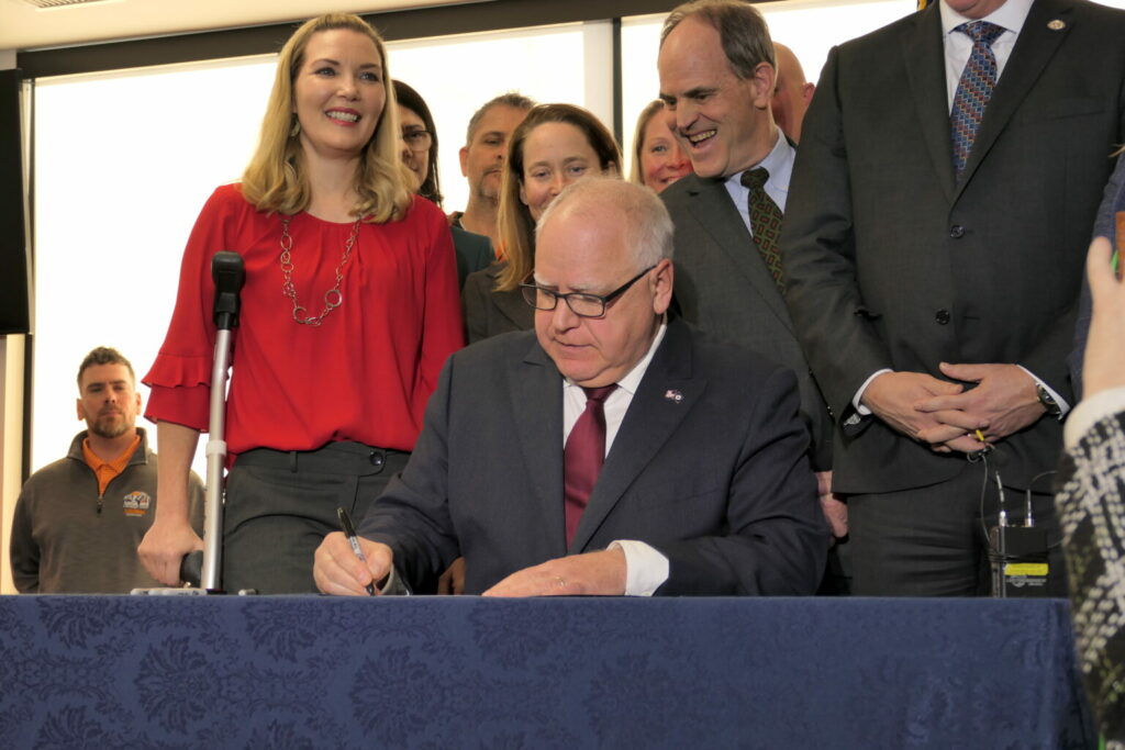 Gov. Tim Walz signing a bill into law at the St. Paul Labor Center, surrounded by supporters.