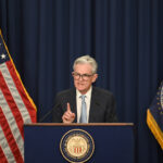 Federal Reserve Chairman Jerome Powell speaks at a press conference about the central bank's decision on interest rates, standing between the American and Federal Reserve flags.