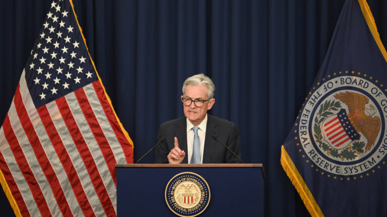 Federal Reserve Chairman Jerome Powell speaks at a press conference about the central bank's decision on interest rates, standing between the American and Federal Reserve flags.