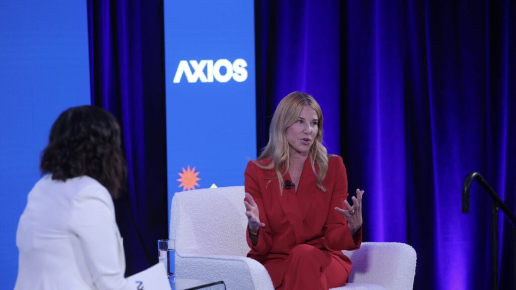 Denise Dresser, CEO of Slack, speaks on stage at the Axios forum, wearing a red suit, discussing workplace communication innovations.