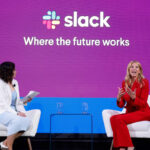 Slack ceo denise dresser speaking on stage with a moderator during a keynote event about the future of work with a large slack logo and tagline in the background