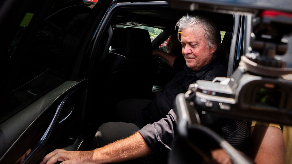 Close-up of a man seated inside a vehicle, with media equipment partially visible in the frame.