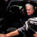 Close up of a man seated inside a vehicle with media equipment partially visible in the frame