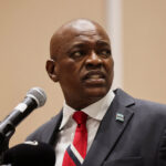 President mokgweetsi masisi wearing a suit and red striped tie speaks into a microphone looking to the side with a serious expression during his concession speech