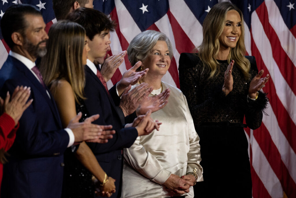 Susie wiles smiles amidst applause standing with family and supporters in front of american flags after her appointment by president trump