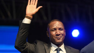 Duma boko wearing a suit and tie raises his hand while giving a victory speech symbolizing his inauguration as botswanas 6th president