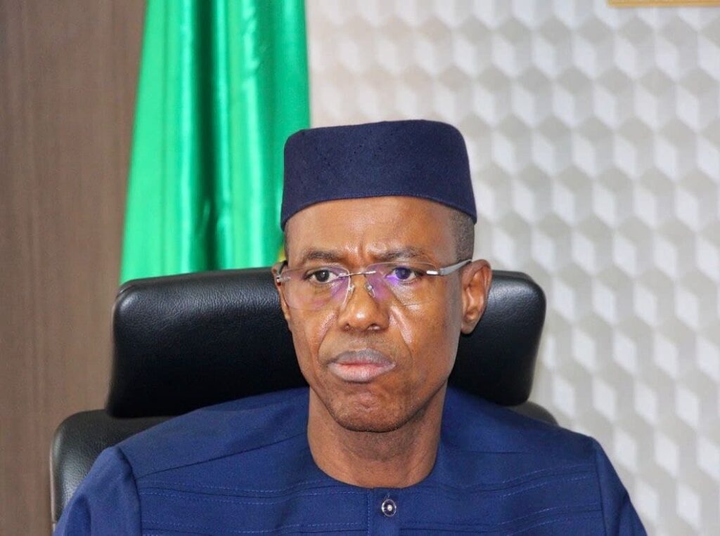 Portrait of malis economy minister alousseni sanou wearing a dark blue traditional outfit seated against a background with a green flag