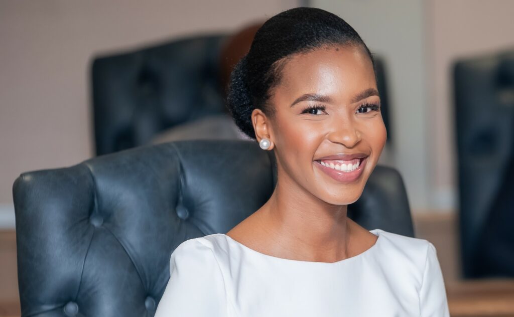 Lesego chombo minister of youth and gender affairs smiling during her appointment ceremony dressed in a white outfit and seated in a formal setting