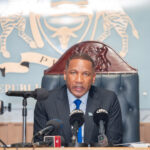 President Duma Boko speaking at a press conference with microphones in front of him, the Republic of Botswana emblem displayed on the wall behind.