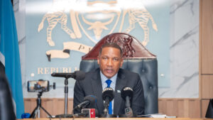 President duma boko speaking at a press conference with microphones in front of him the republic of botswana emblem displayed on the wall behind