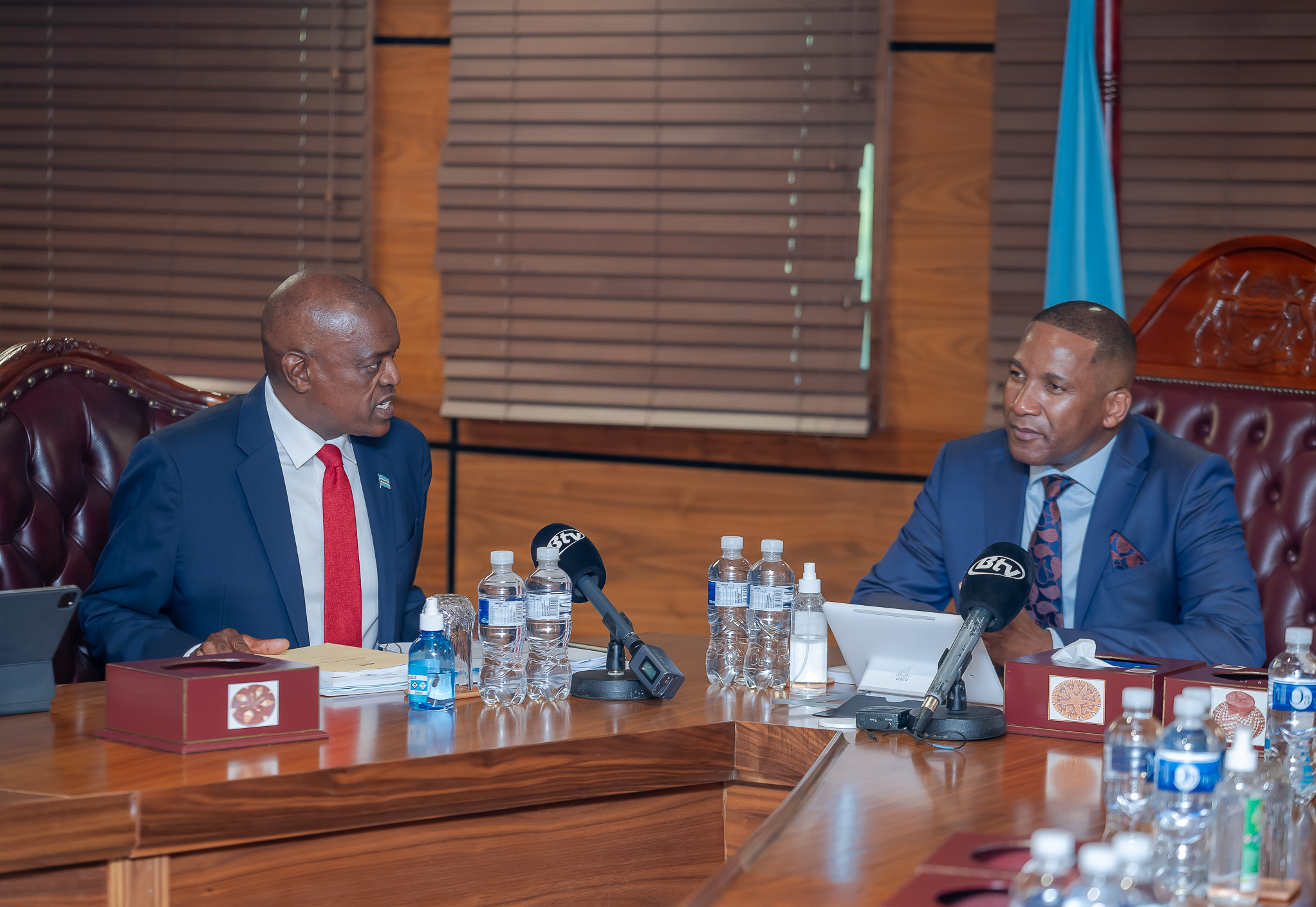 President Mokgweetsi Masisi and President-elect Duma Boko in discussion during the handover ceremony, with microphones and documents on a wooden conference table.