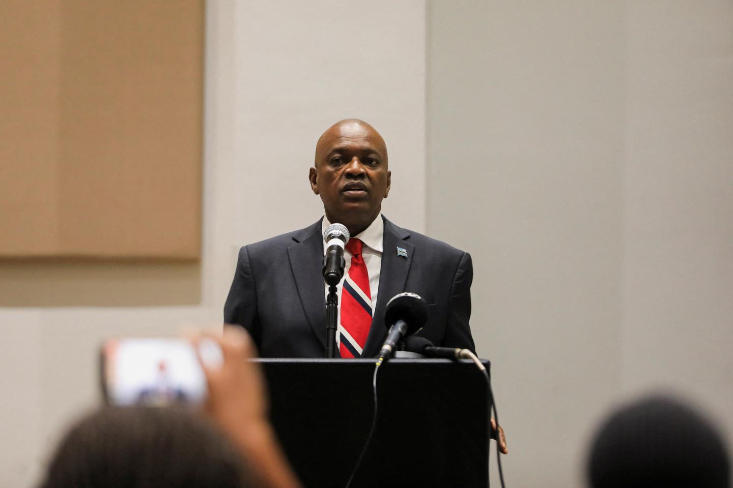 President Masisi delivering a concession speech at a podium, wearing a dark suit and red tie, with microphones placed in front of him.