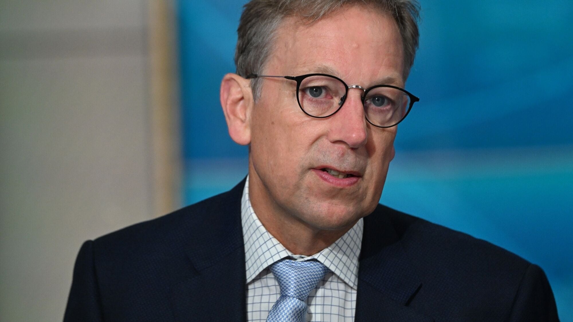 Jakob Stausholm, CEO of Rio Tinto, wearing glasses, a dark suit, and a patterned tie, speaking during an interview with a blue background.