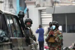 Armed m23 rebel fighters in camouflage uniforms and tactical gear stand near a military vehicle one holding a radio for communication amid ongoing clashes in goma drc