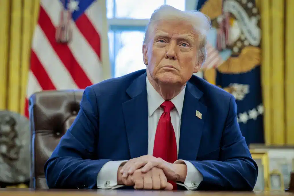 President donald trump in the oval office dressed in a navy suit and red tie making a statement on trade tariffs against mexico canada and china