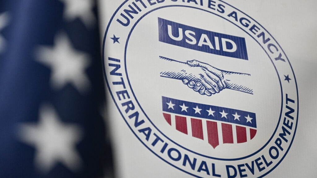 Usaid logo on a banner featuring a handshake symbol and patriotic red white and blue colors representing u S International development efforts