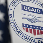 Usaid logo on a banner featuring a handshake symbol and patriotic red white and blue colors representing u S International development efforts