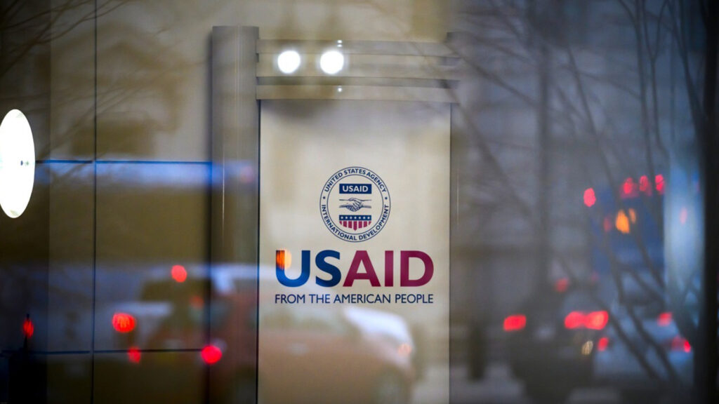 A glass entrance of the usaid headquarters in washington d C  displaying the agencys logo and slogan from the american people 