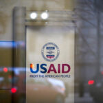 A glass entrance of the USAID headquarters in Washington, D.C., displaying the agency's logo and slogan "From the American People."