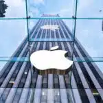 Looking up at apples glass storefront on fifth avenue with the apple logo and skyscrapers reflecting in the glass