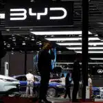 People viewing byd electric vehicles at an auto expo under a brightly lit byd logo