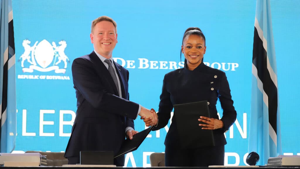 De beers ceo and bogolo kenewendo shaking hands after signing the de beers   botswana partnership agreement standing in front of a backdrop featuring the republic of botswana and de beers group logos