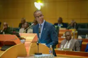 Ndaba gaolathe dressed in a navy blue suit and tie speaks at a podium in parliament while delivering botswanas 202526 budget speech with government officials seated in the background