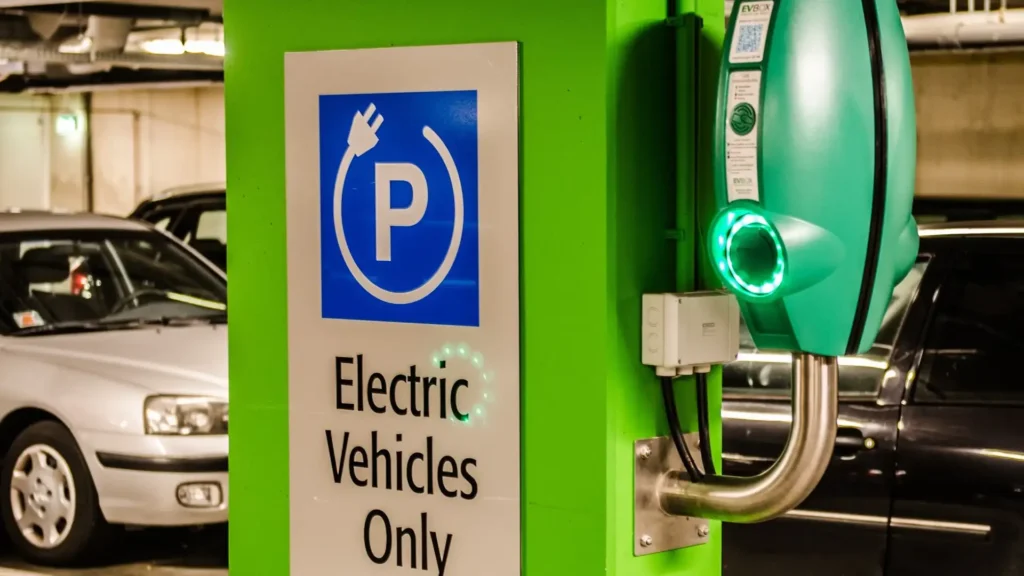 Electric vehicle charging station in an underground parking garage with a green pillar and "Electric Vehicles Only" sign.
