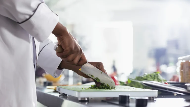 Chef chopping herbs on a cutting board in a professional kitchen.