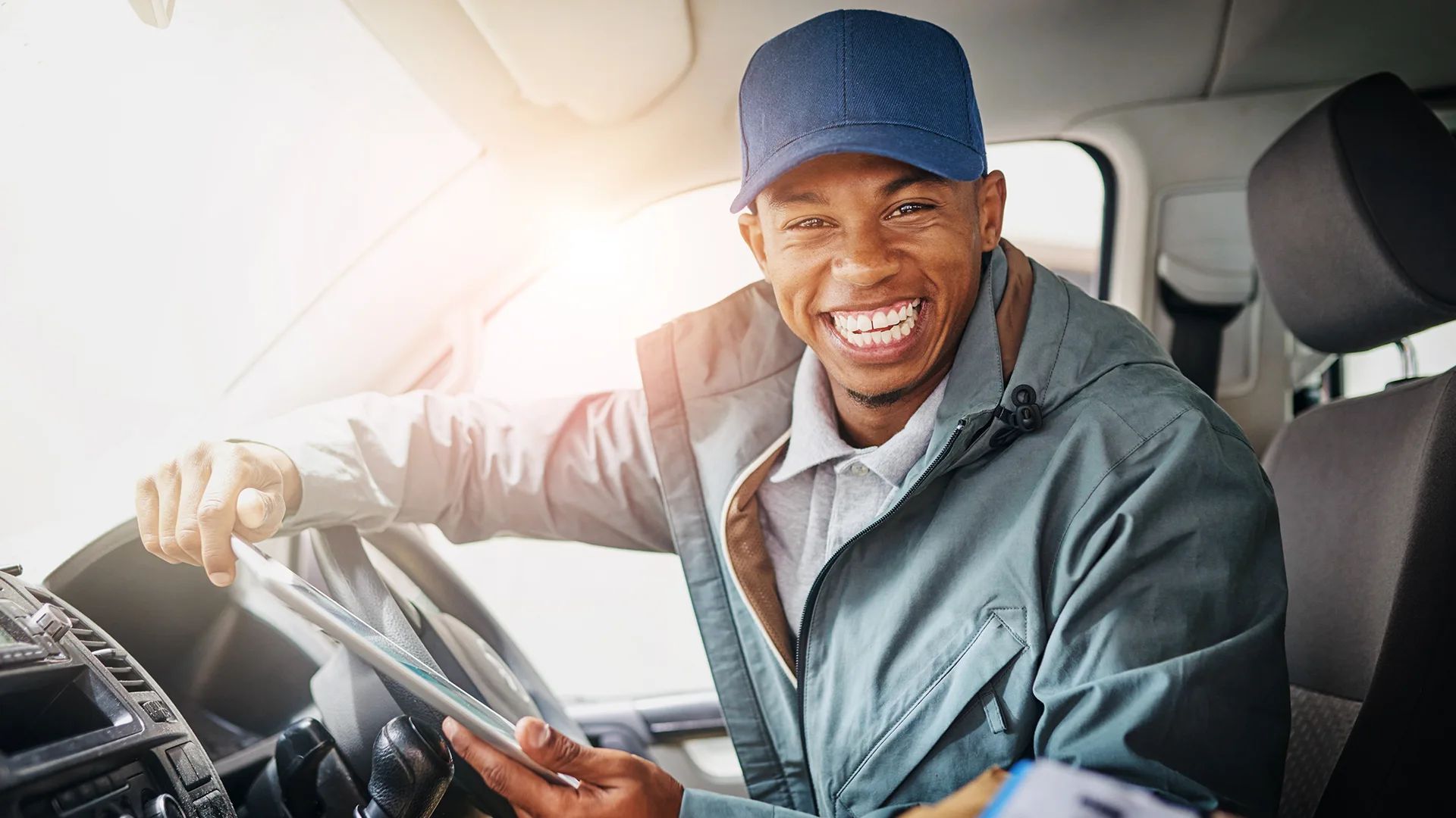 Smiling driver holding a tablet inside vehicle cabin.