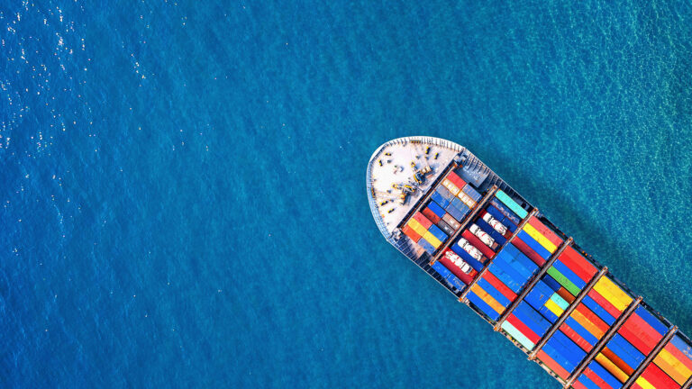 Top-down aerial view of container ship sailing on clear blue water.