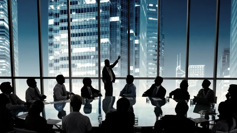 Business leader presenting to a board of executives in a modern high-rise conference room overlooking a city skyline at night.